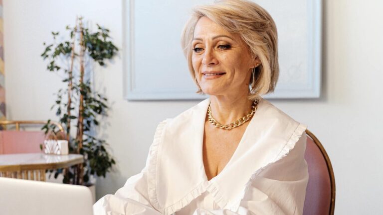 Elderly woman smiling and typing on a laptop in a chic and modern workspace.